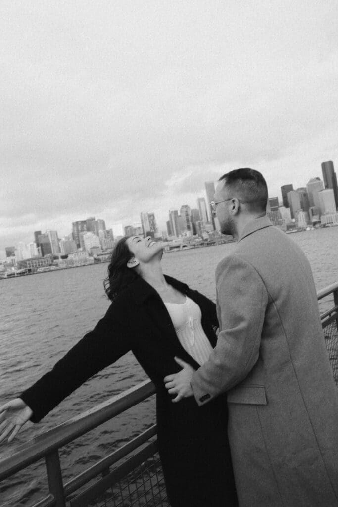 Black and white photos of a woman leaning backwards over the rail of the Seattle-Bainbridge ferry while her fiance holds her by the waist