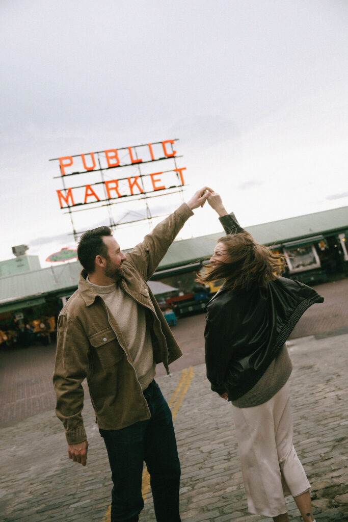 Man twirling woman in the street in front of the Pike Place Market sign