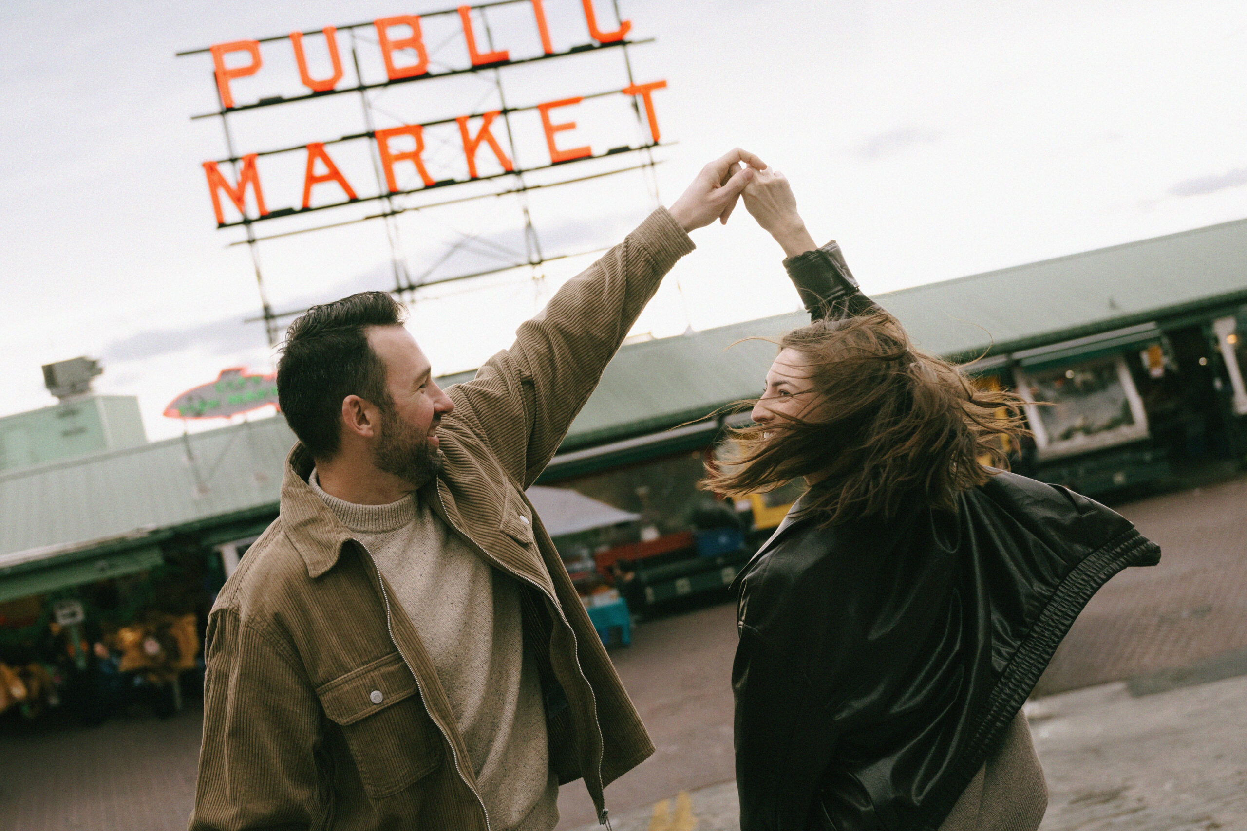 Man twirling woman in the street in front of Pike Place Market sign