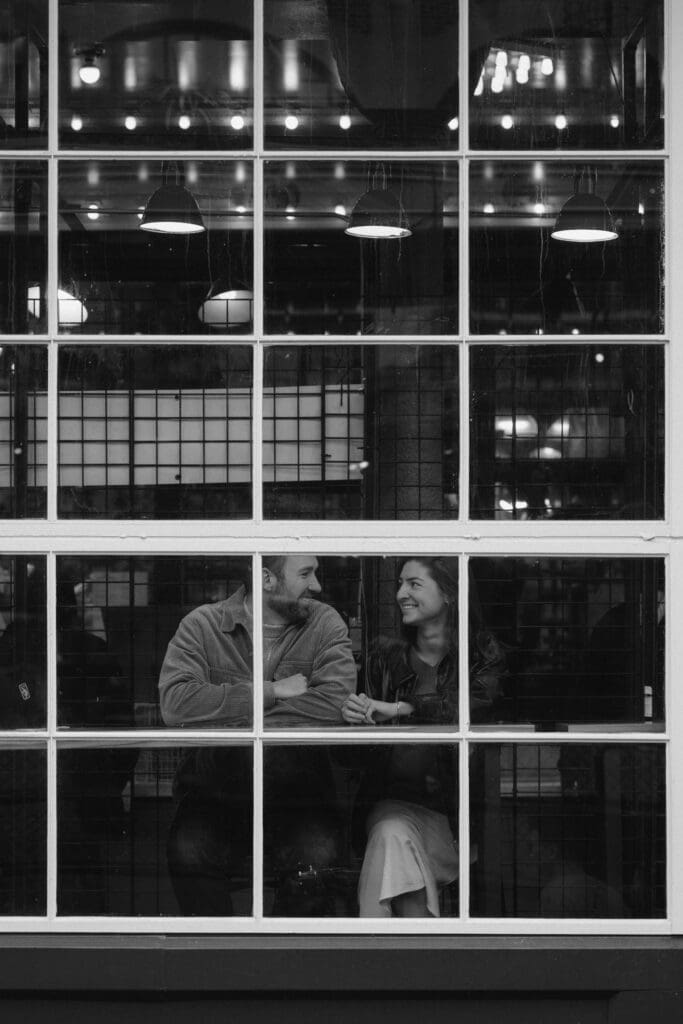 Black and white photo of a couple sitting in the window of a coffee shop