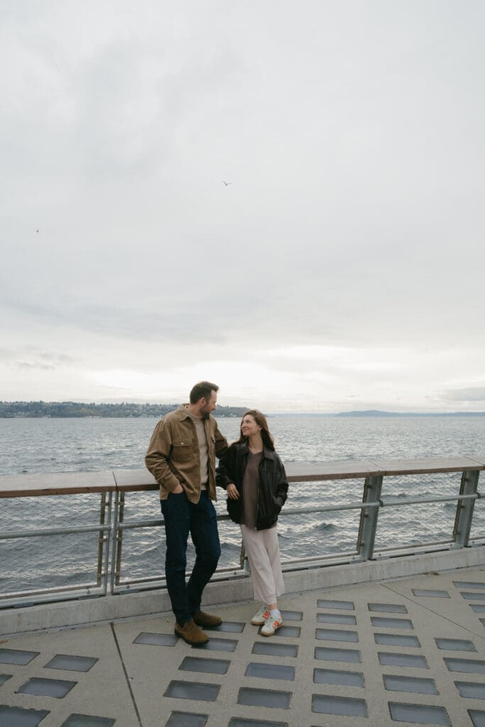 Couple leaning against the railing of a pier with Puget Sound in the background