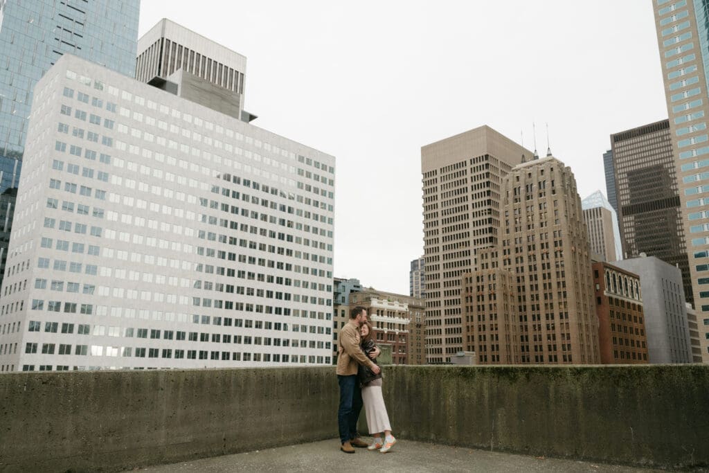 Couple embracing on a parking garage rooftop with city in the background