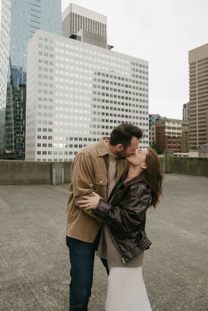 Couple kissing on a parking garage rooftop with city in the background