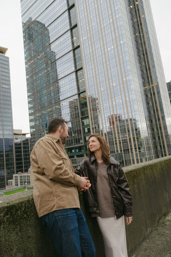 Couple leaning against a wall talking to each other with skyscraper in the background