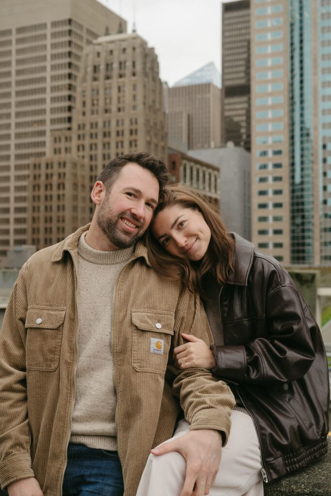 Engaged couple smiling with city in the background