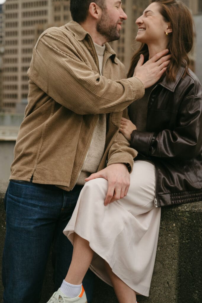 Man and woman smiling at each other sitting on a wall