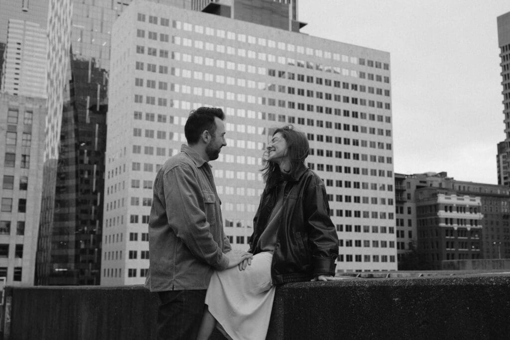 Black and white photo of a couple smiling at each other on a parking garage rooftop in Seattle