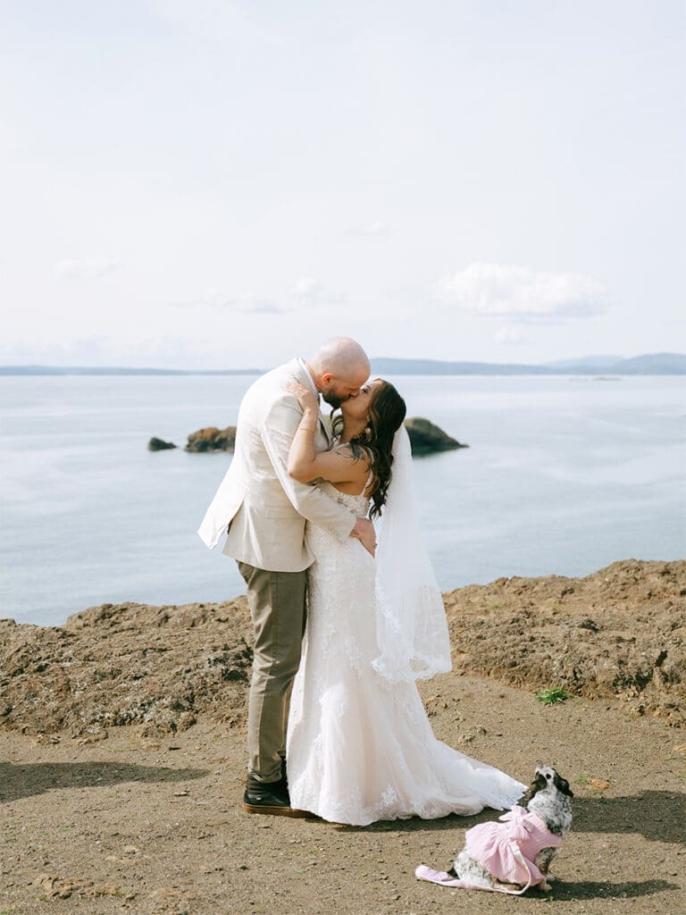 A couple in wedding attire kissing on cliffs above water at their Deception Pass elopement