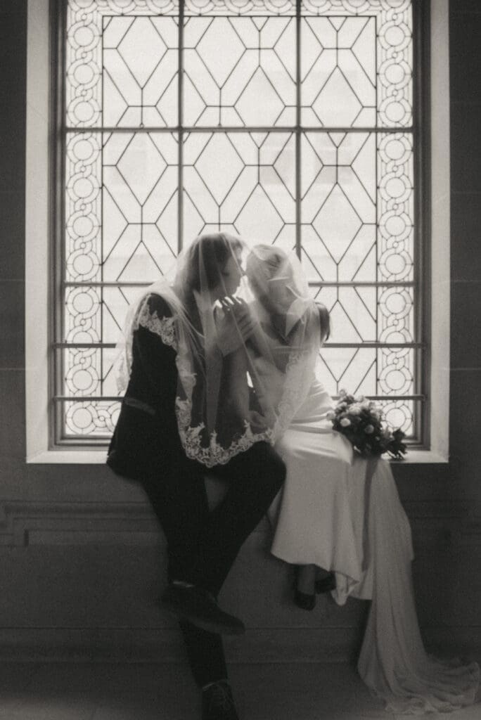 A couple in wedding attire sitting on the windowsill in San Fransisco City Hall