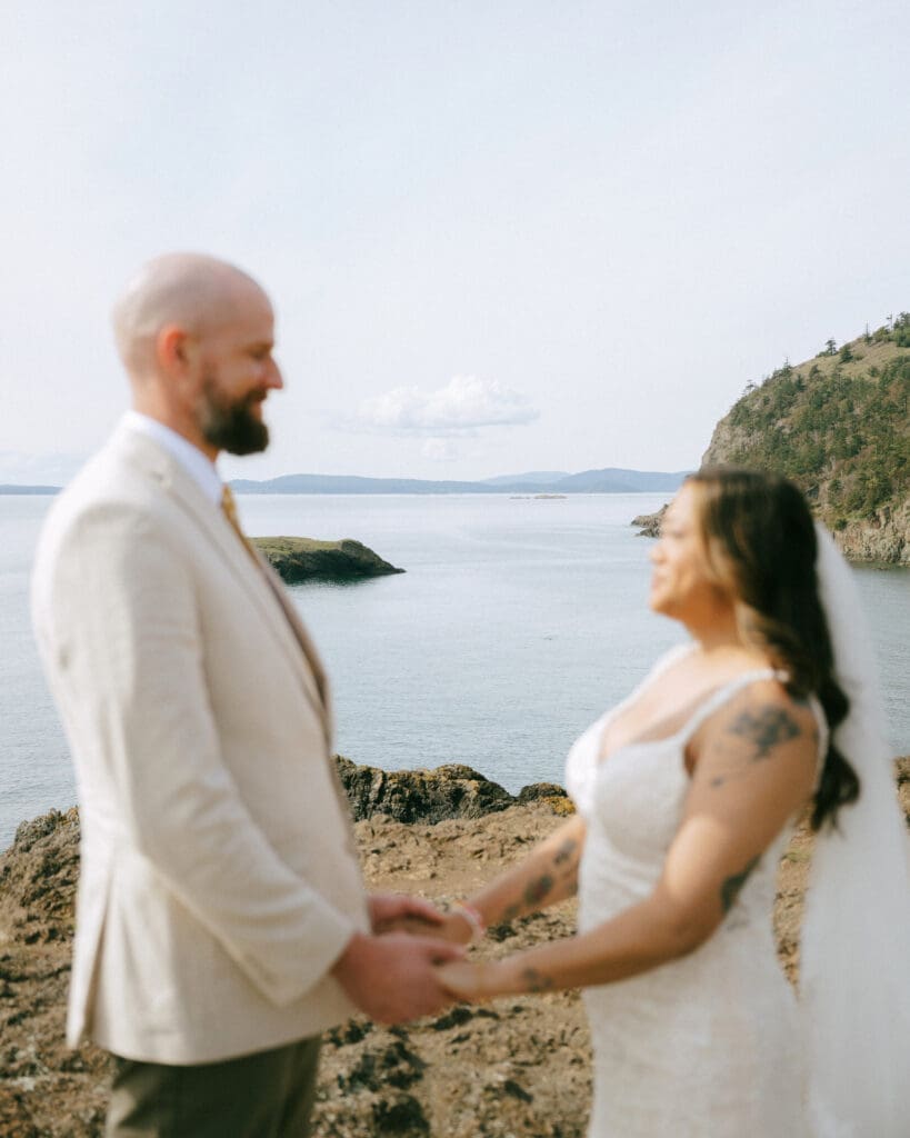 A couple in wedding attire standing on cliffs above water at their Deception Pass elopement