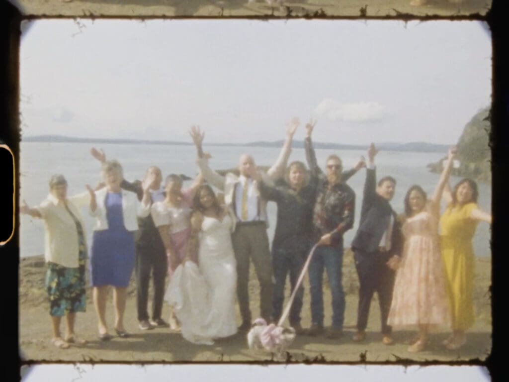 Super8 photo of a couple in wedding attire and their families standing on cliffs above water at their Deception Pass elopement