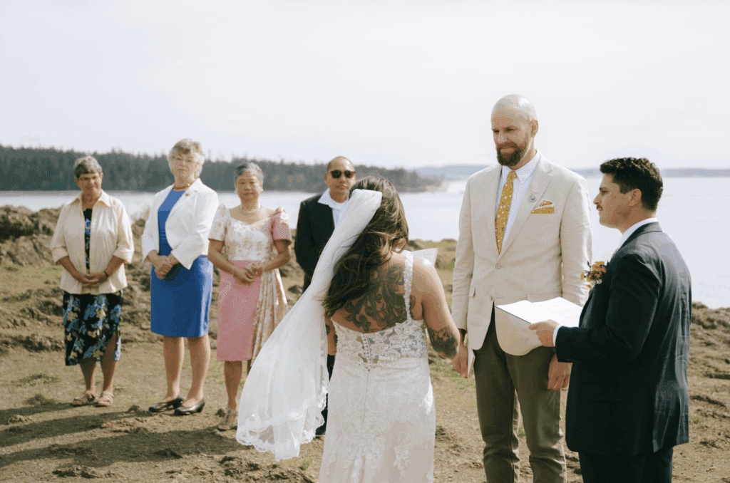 A couple in wedding attire and their families standing on cliffs above water at their Deception Pass elopement