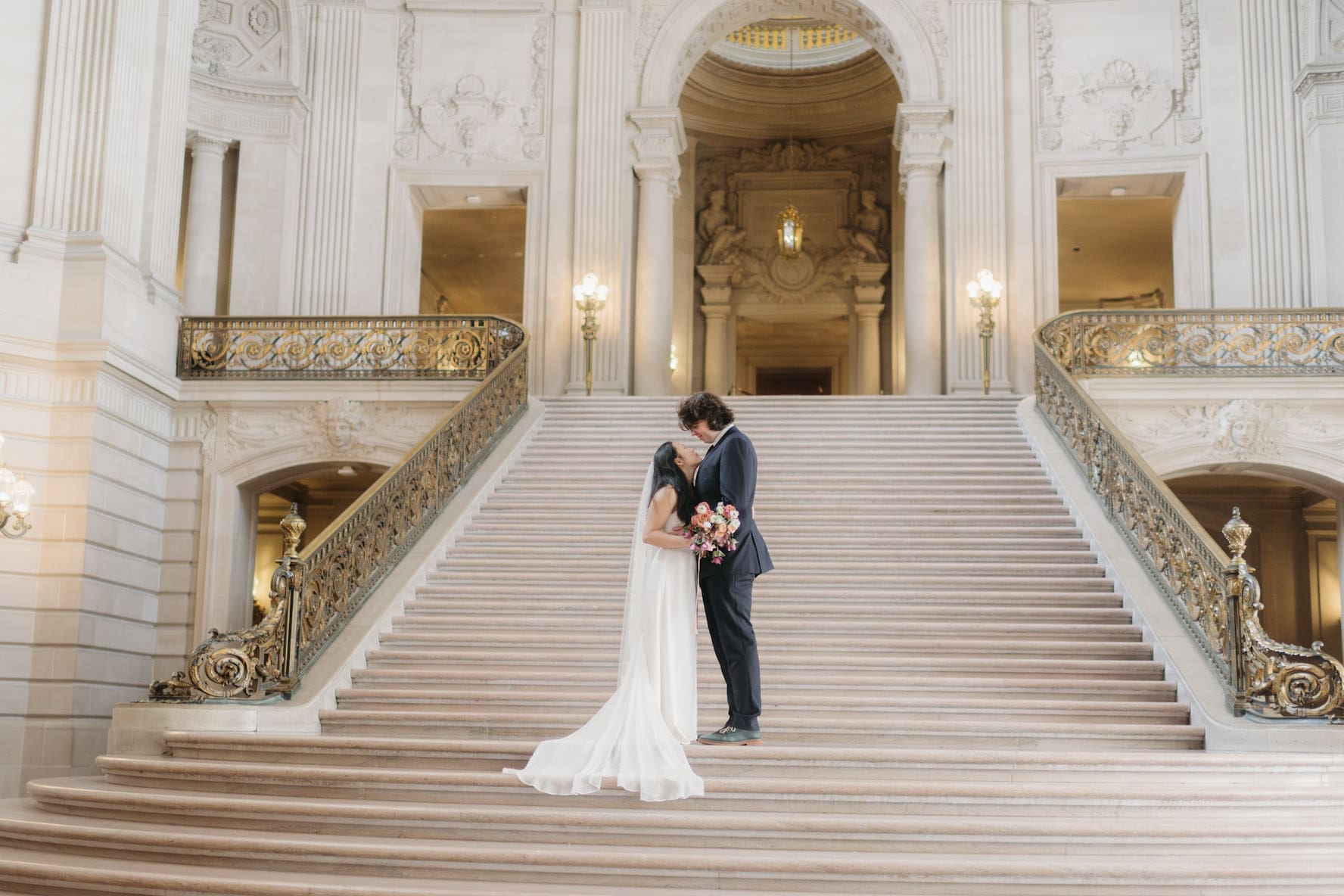 A couple in wedding attire standing on the grand staircase of San Fransisco City Hall